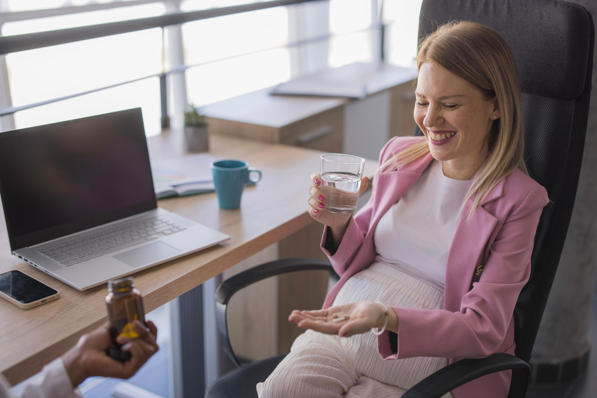 Pregnant woman taking vitamins for prenatal health at work