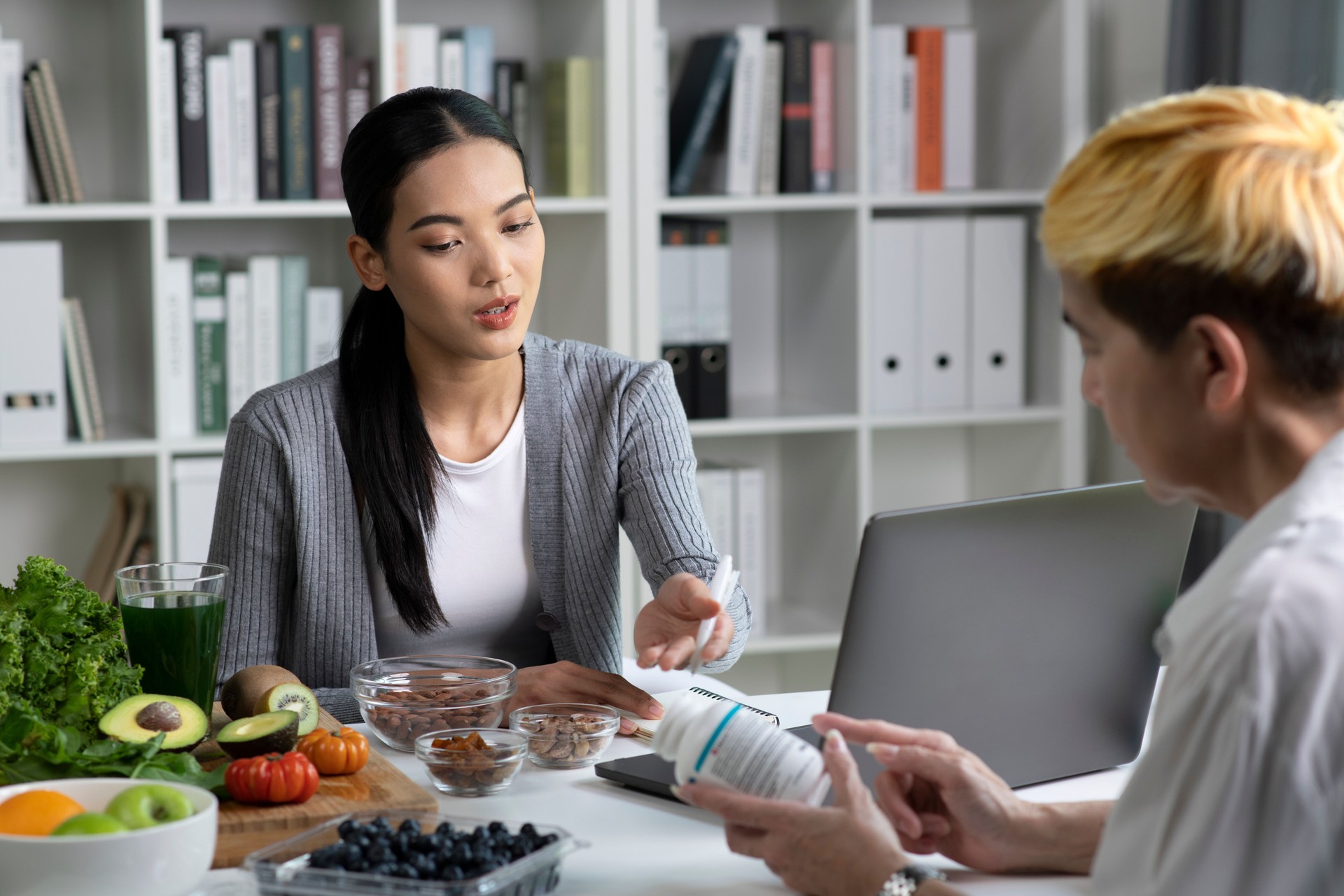 Woman Asian Professional Nutritionist consulting with her client, surrounded by a variety of fruits, nuts, vegetables, and dietary supplements on the table